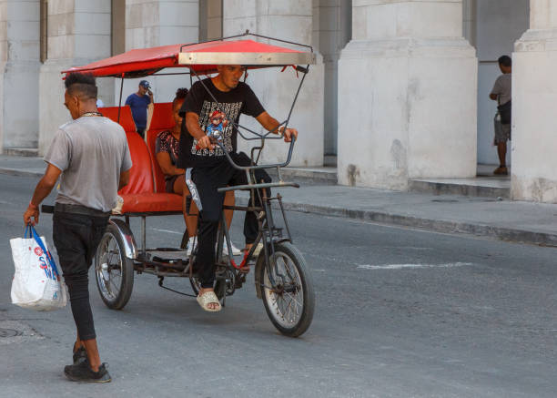 Havana, Cuba - August 10, 2024: A Cuban man drives a bici-taxi on a city street. Another man walks with a bag