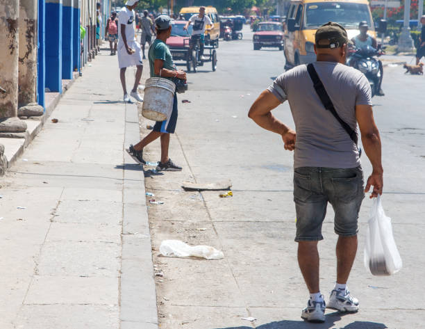 Havana, Cuba - August 7, 2024: A Cuban man walks with a platic shopping bag on the sidewalk. Another one carries a plastic bucket. City life in the downtown district.