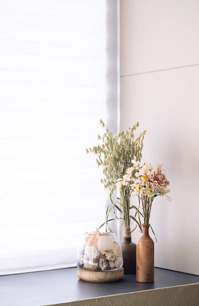 istock Dried floral arrangement and seashells in rustic vases on windowsill by window. 2166485180