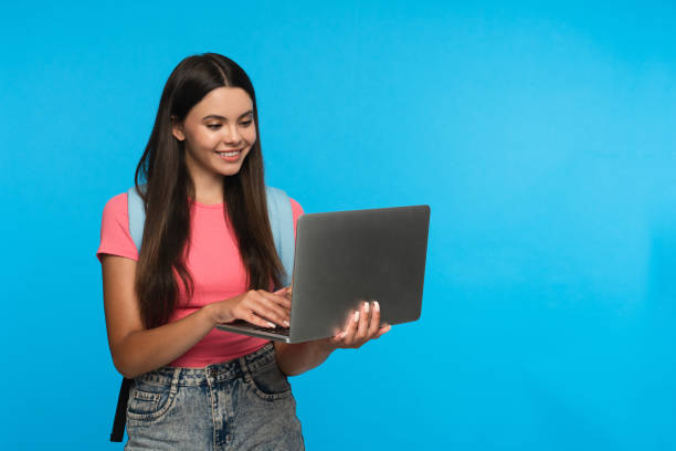 istock Smiling girl using laptop for distant studding doing homework online isolated in blue background 2166488276