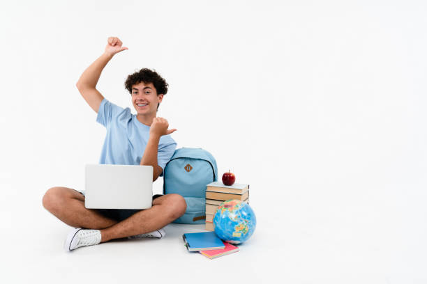 istock Smiling boy pupil student teenager using laptop points index fingers copy space isolated background. 2166489067