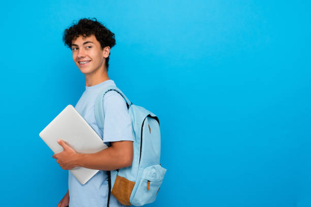 istock Boy pupil student in casual with backpack holding laptop copy space isolated on blue background 2166489356