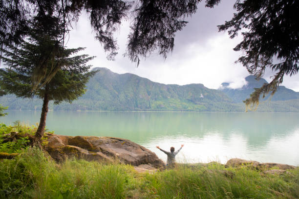 Woman stands on beach, tranquil bay, forest and mountains
