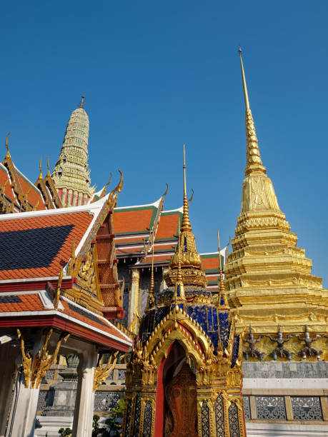 A mesmerizing low-angle perspective captures a Thai temple in all its glory: resplendent red roofs, gleaming gold details, and a majestic white pinnacle, all framed by a flawless blue sky.