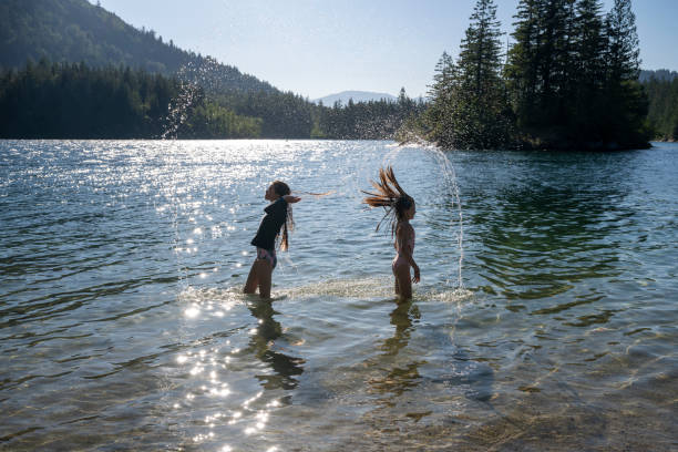 Young girls play in lake below mountains and forest, Harrison Hot Springs, B.C.