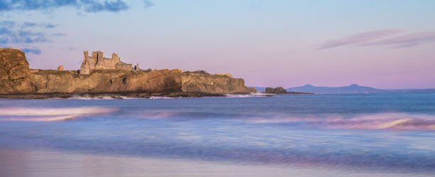 Tantallon Castle, Scotland, on a cliff by the sea at sunrise, with pink sky reflected in the water Ruins of Tantallon Castle from Seacliff beach, near North Berwick, Scotland, on a cliff by the sea at sunrise, with waves crashing on beach and pink sky reflected in the water north berwick scotland east lothian castle scotland stock pictures, royalty-free photos & images