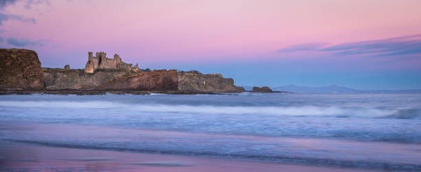 Tantallon Castle, Scotland, on a cliff by the sea at dawn, with pink sky reflected in the water Ruins of Tantallon Castle from Seacliff beach, near North Berwick, Scotland, on a cliff by the sea at dawn, with waves crashing on beach and pink sky reflected in the water north berwick scotland east lothian castle scotland stock pictures, royalty-free photos & images