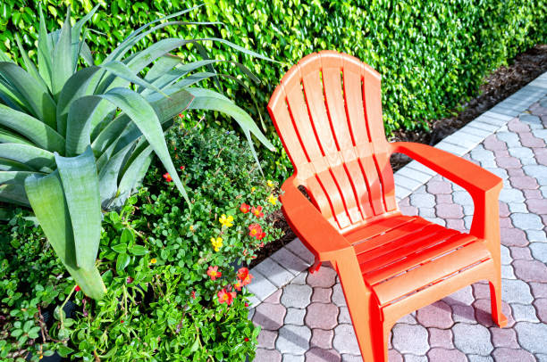Chair on pavers with a hedge and potted plant.