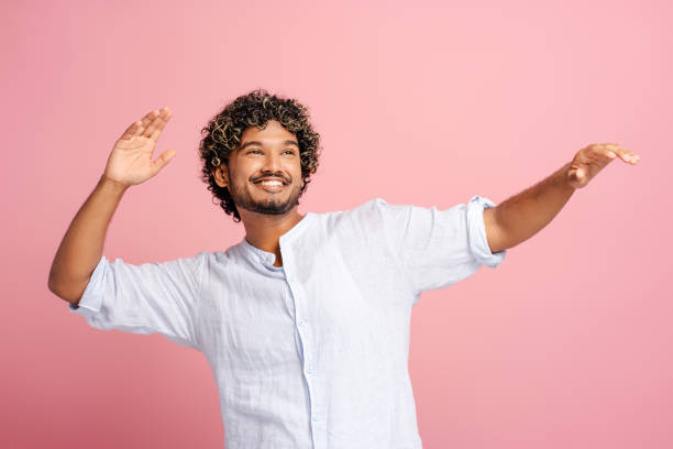 istock Smiling, handsome man presenting something with open arms on pink background 2166513365