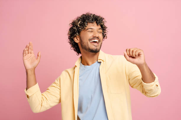Carefree young man is dancing and having fun on pink background