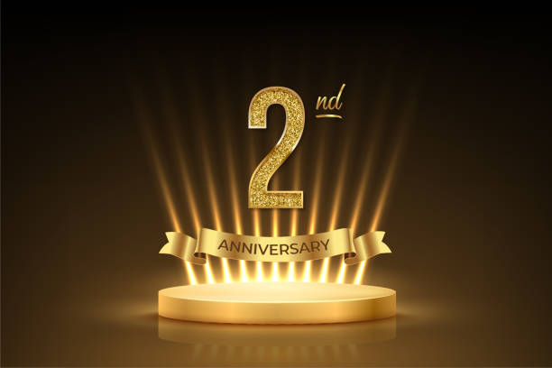istock Second anniversary gold award podium. 2 year celebration birthday or jubilee golden vector background. Luxury stage with glowing rays, glittering number 2 and ribbon with text anniversary on black 2166524158