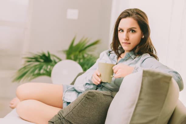 istock Woman sitting with green mug, thoughtful expression 2166536524