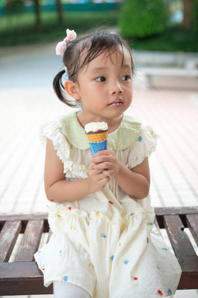 istock Girl sitting on bench enjoying ice cream cone, with thoughtful expression. 2166550875