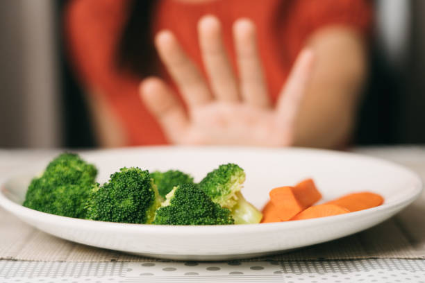 Little cute kid girl refusing to eat healthy vegetables. Children do not like to eat vegetables. stock photo