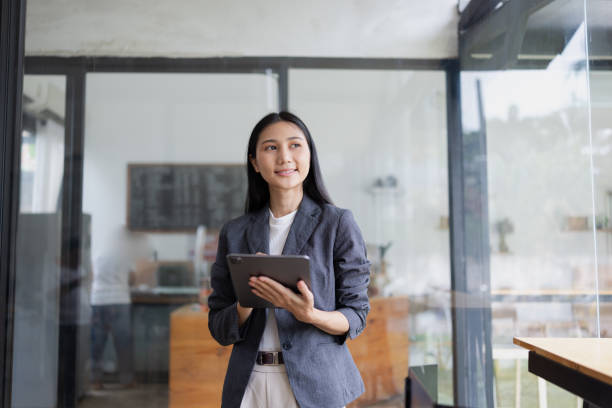 istock Smiling  asian woman holding a tablet standing in office. 2166553382