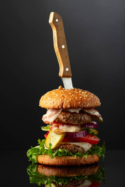 istock Fresh tasty burger with knife on a black reflective background. 2166557692