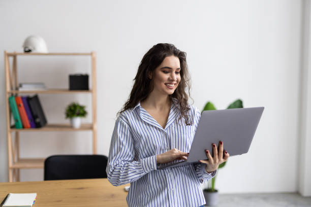 istock Beautiful young business woman wearing shirt using laptop while standing in modern workspace 2166566401