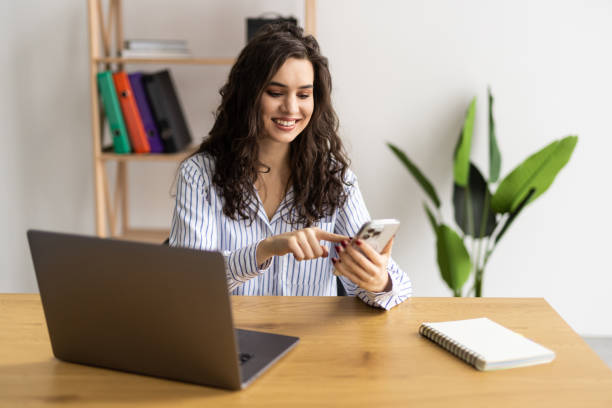 istock Young woman smiling and using cellphone during offline meeting in office 2166566695