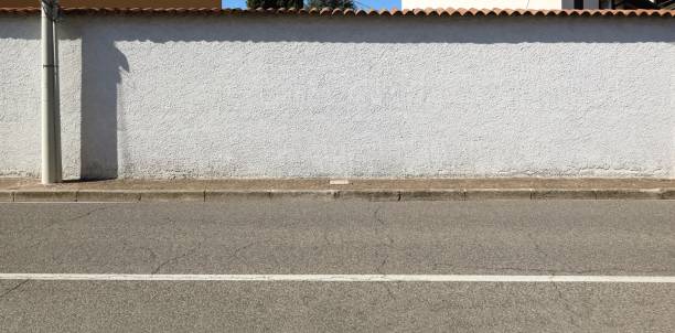 Long white stucco surrounding wall with rooftiles on top. Sidewalk and street in front.