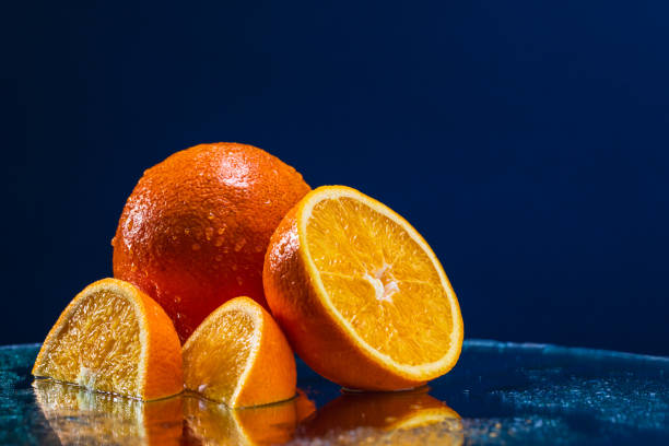An artistic composition featuring whole and sliced oranges elegantly arranged on a mirror-like surface. The reflective backdrop adds depth and an abstract quality to the image, making it ideal for modern food photography, creative advertising campaigns, and design projects that require a unique and visually striking element. The vibrant colors and abstract reflection capture attention, making this image perfect for various creative uses