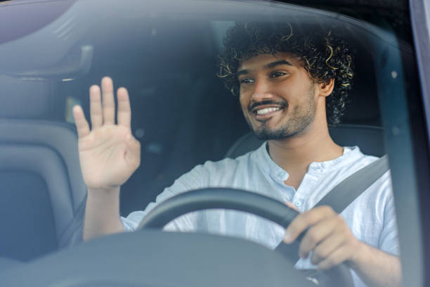 istock Young man is driving a car and waving to someone 2166572565