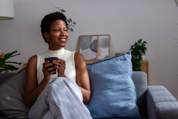 istock Young black woman relaxing on sofa drinking coffee and smiling 2166572916