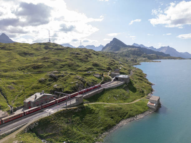 istock Red Train Stationed Alongside Alpine Lake in Mountainous Terrain 2166573065
