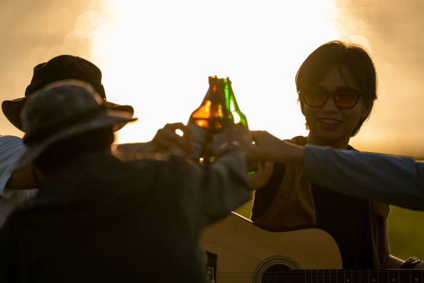 Three people are holding up beer bottles and smiling at the camera. Scene is happy and celebratory