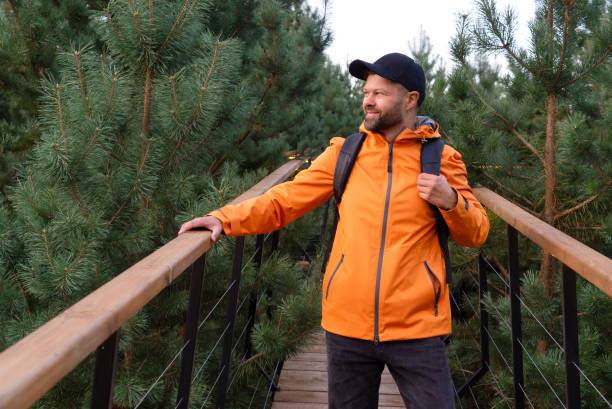 istock Backpacker in orange jacket standing on wooden path in scandinavian forest 2166575037