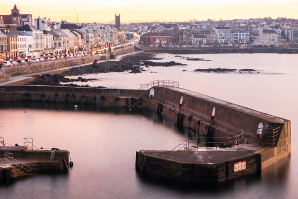 Portstewart, UK - December 27th, 2021: Sun beginning to set with pink tones on surface of water in harbour and expansive view across the town.