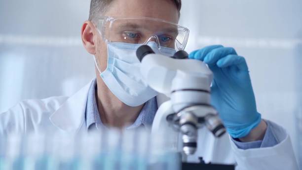 istock Man scientist with protective glasses, mask and gloves is using microscope in laboratory, portrait of researcher. Microbiology science concept 2166582818