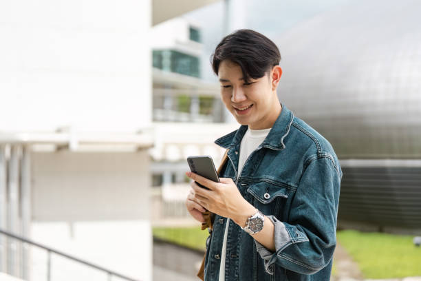 istock Happy College Student Using Smartphone Outdoors on Campus in Casual Denim Jacket 2166583212