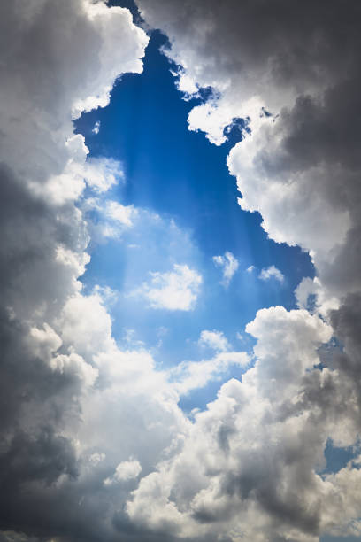 Blue sky with white cumulus clouds and a break through which rays of light shine, vertical shot