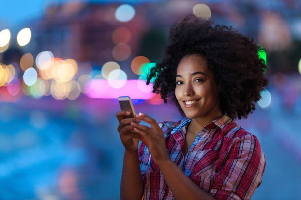 istock Smiling woman using phone with city lights behind 2166588182