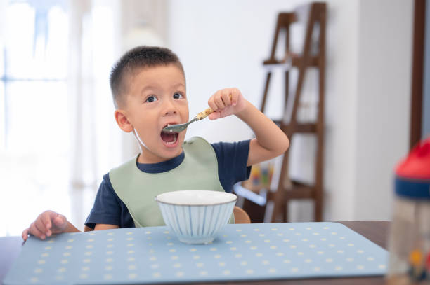 istock Boy raising spoon with food in hand while smiling at the camera brightly. 2166591101