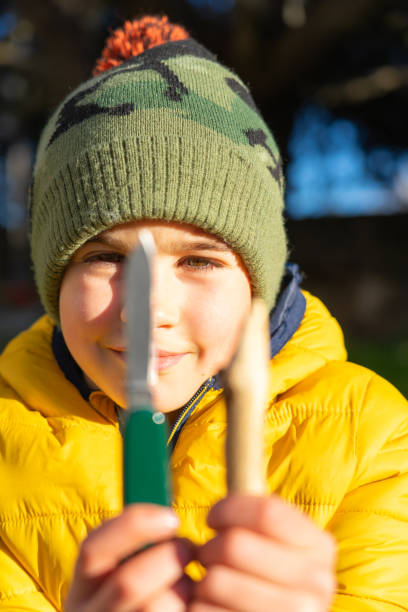 Boy explorer showing his knife and the stick he has sharpened in a survival workshop for children in nature