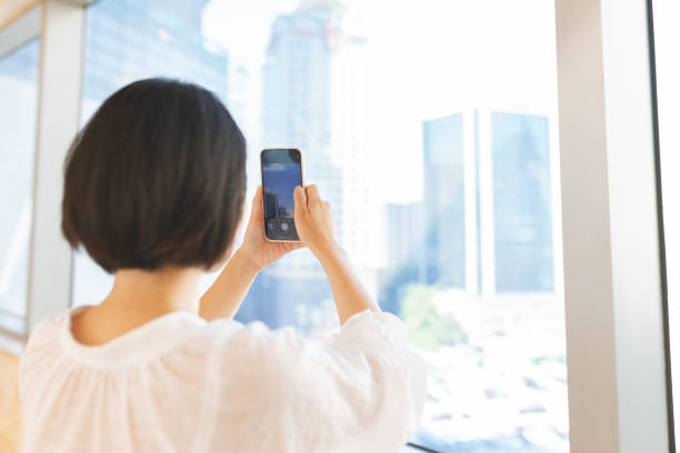 istock Asian woman using mobile phone near window 2166593604