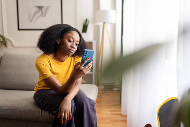 istock Sad woman in yellow shirt using phone while sitting on couch. 2166596410