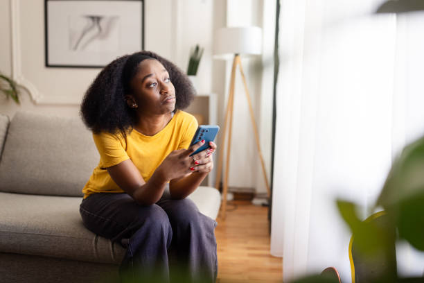istock Sad woman sitting on couch using phone by window indoors. 2166596454