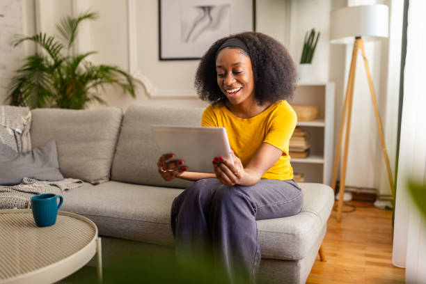 istock Woman holding tablet and laughing, sitting on couch. 2166600174