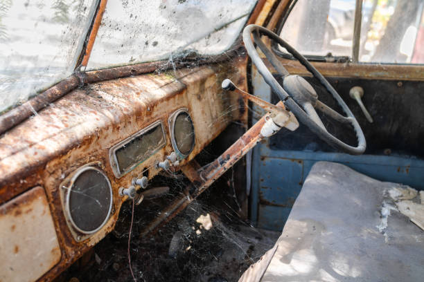 Abandoned old rusty car interior with dashboard and steering wheel covered with cobweb