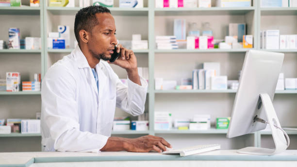 istock Multiracial male pharmacist, checking medicine on a computer and talking on the phone at a pharmacy. Multiracial pharmacist working in drugstore at a pharmacy. 2166601625