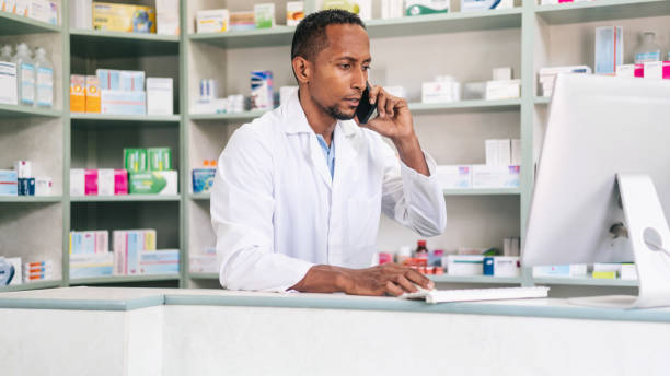 istock Multiracial male pharmacist, checking medicine on a computer and talking on the phone at a pharmacy. Multiracial pharmacist working in drugstore at a pharmacy. 2166601629