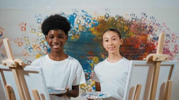 istock African boy and caucasian girl look at camera while paint canvas. Edification. 2166604924