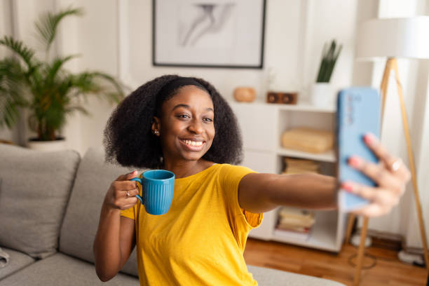 istock Woman smiling while taking selfie with phone and mug 2166606574