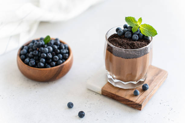 istock Delicious chocolate mousse or pudding with chocolate cookie crumbs, fresh blueberry and mint on a light concrete background. Confectionery menu, glass dessert recipe. 2166608868
