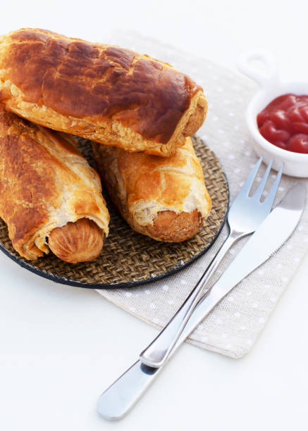 Rolled Hot Dog Sausages Baked in Puff Pastry with Cutlery and Ketchup on White background