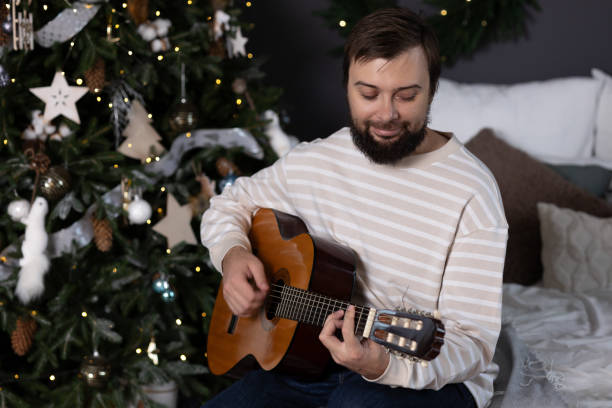 istock Man playing guitar by christmas tree 2166610932