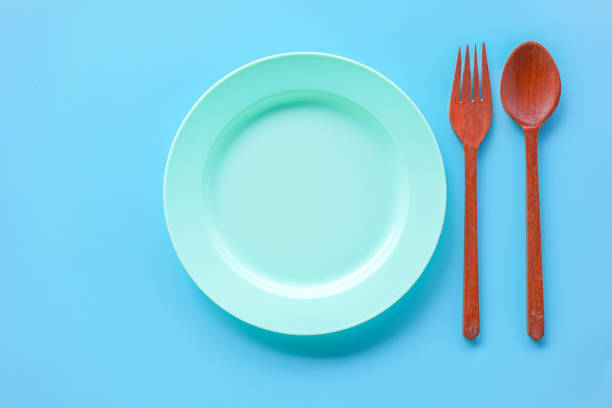istock Flat lay view of empty green plastic dish with wood spoon and fork on blue background 2166611956