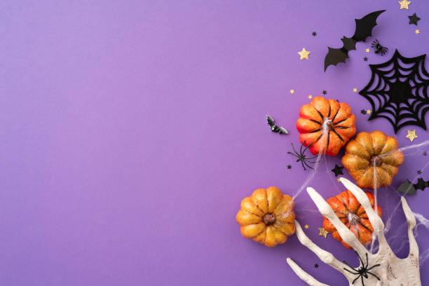 istock Festive Halloween background on a purple backdrop featuring pumpkins, spider, bats, star confetti, and a spooky skeleton hand 2166615848